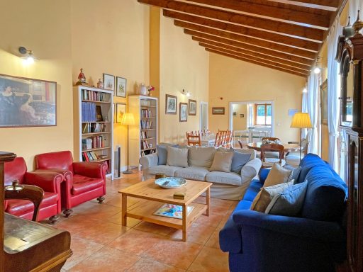 Sala amplia con sofás, sillas, mesas y paredes de color claro y vigas de madera.